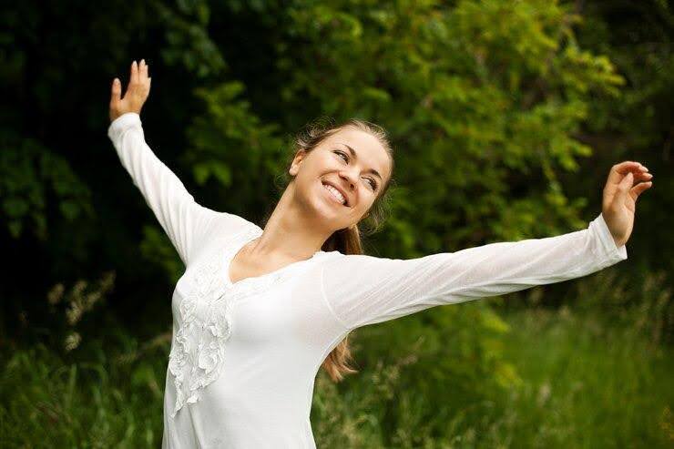 a woman in a white long sleeve shirt is stretching her arms outdoors